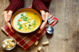 Hands holding bowl of vegetable soup